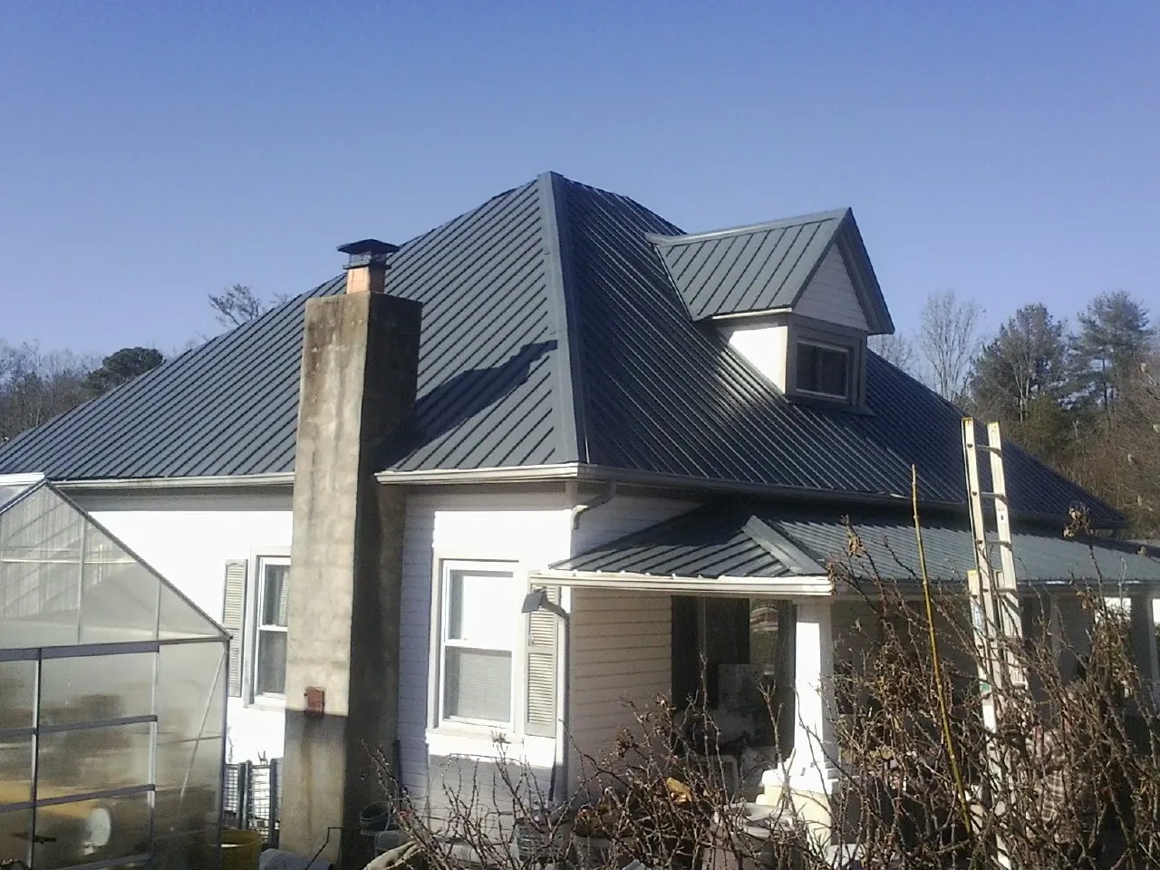Dark blue standing seam metal roof on a white farmhouse with dormer — Slate & Tile Roof Repair by Roofing Brothers in Erath