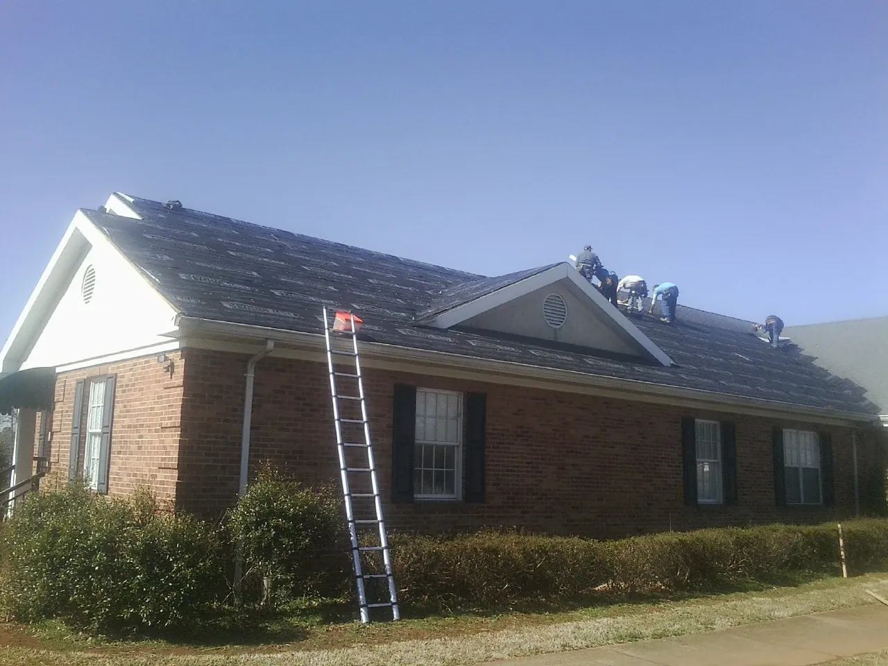 Crew tearing shingles off a brick ranch roof with a ladder set — Emergency Roof Repair work by our crew in Erath