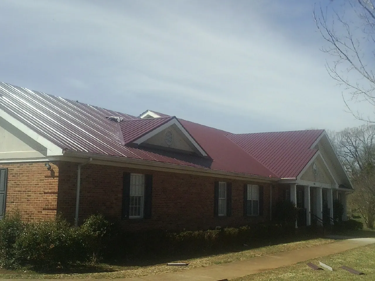 Red metal roof with gabled entries on a long brick building, from a Hail Damage Roof Repair job in Erath