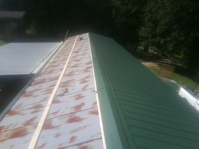 Old rusted panels beside newly installed green metal roofing — Wind Damage Roof Repair by Roofing Brothers in Erath