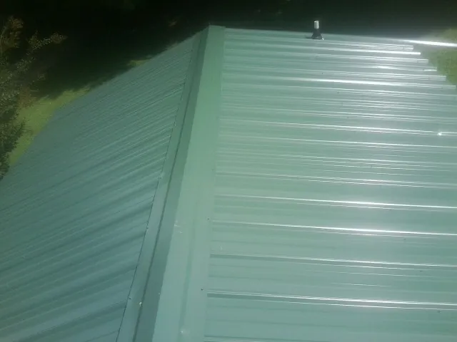 New green metal panels meeting at the ridge of a roof — Flat Roof Repair work by our crew in Erath