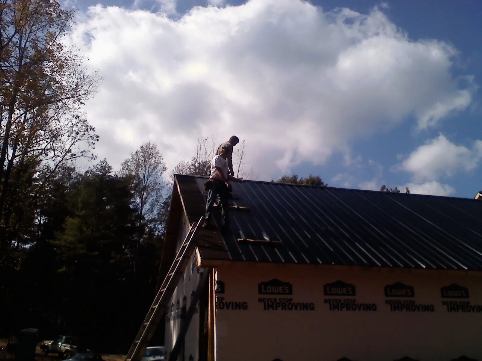 Roofer fastening dark metal panels high against a cloudy sky, from a Roof Inspection job in Erath