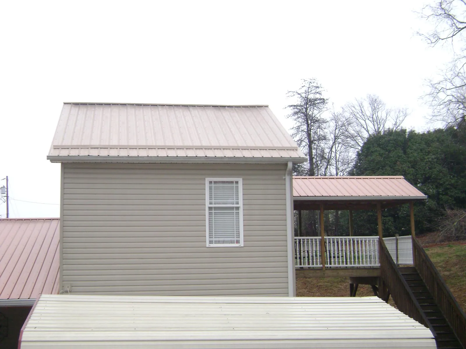 Tan metal roofs on a two story addition and attached porch, from a Roof Replacement job in Erath